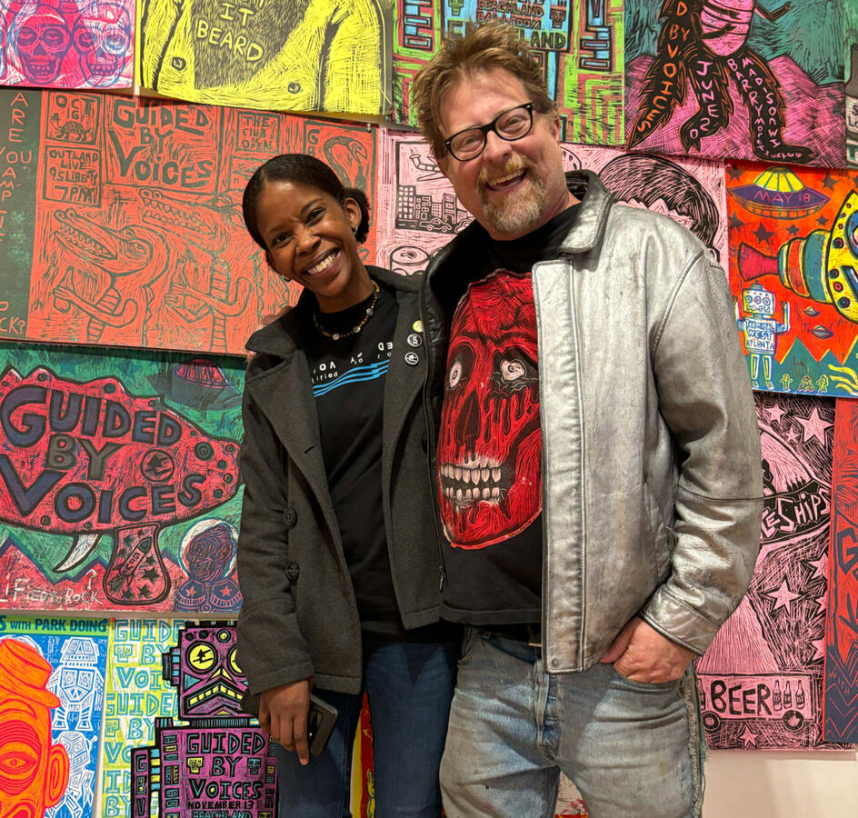 Two people smiling in front of Guided by Voices art installation at Blue House Gallery